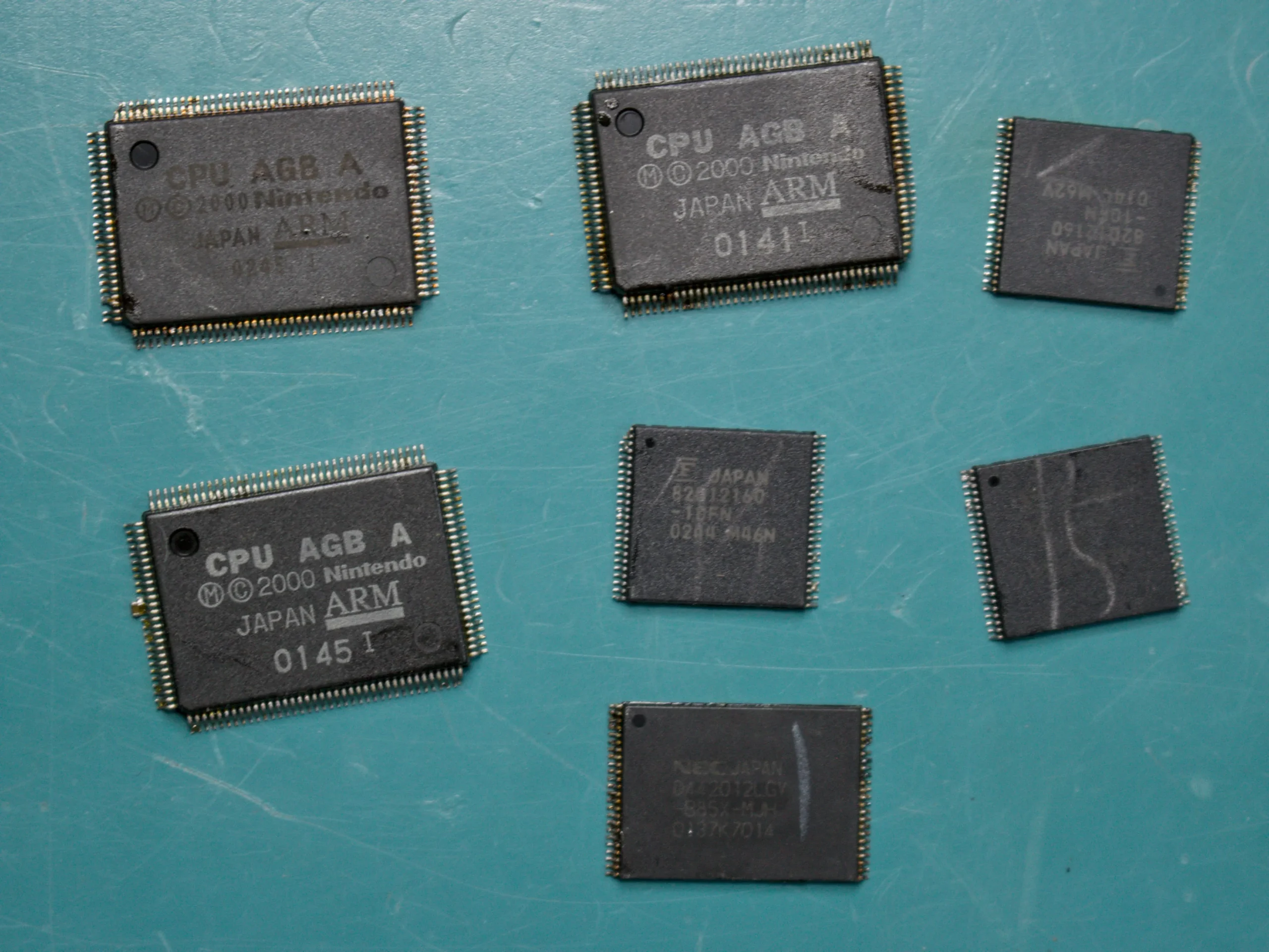 Assorted Game Boy Advance CPU and memory chips removed from donor boards on a blue work mat