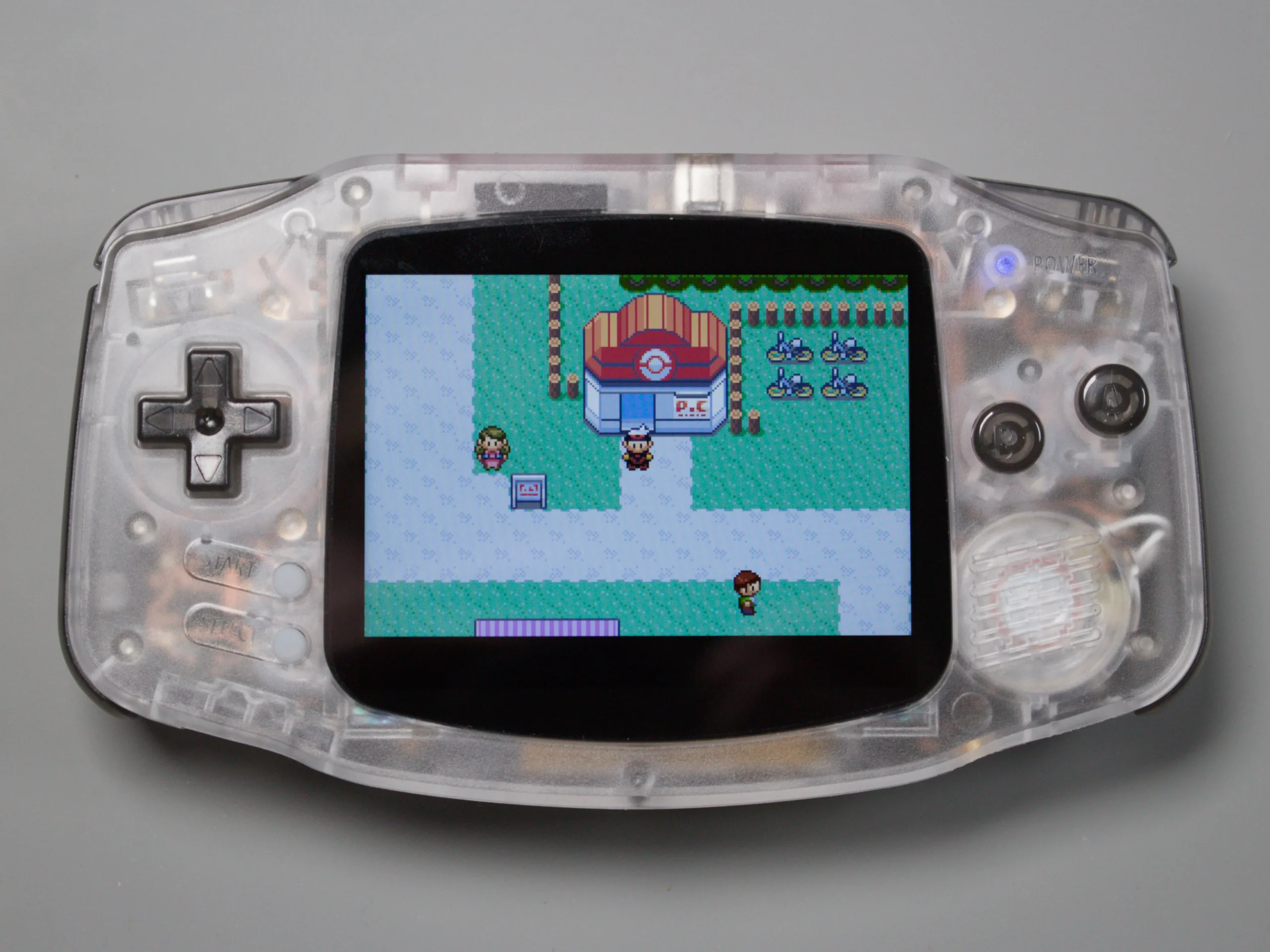 Clear-shell Game Boy Advance powered on and displaying a Pokémon game