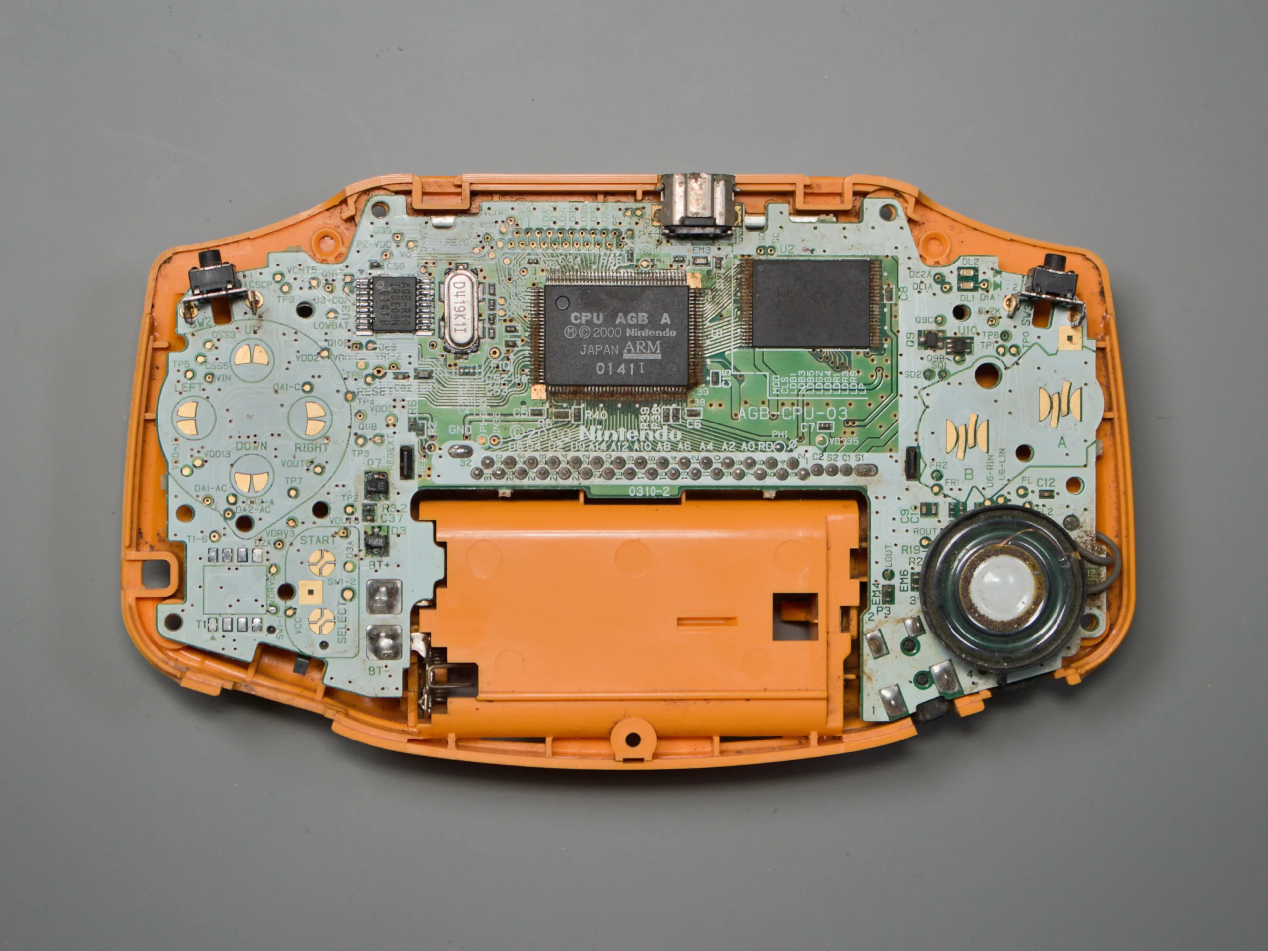 Open orange Game Boy Advance showing the front side of the motherboard, CPU, memory, and speaker