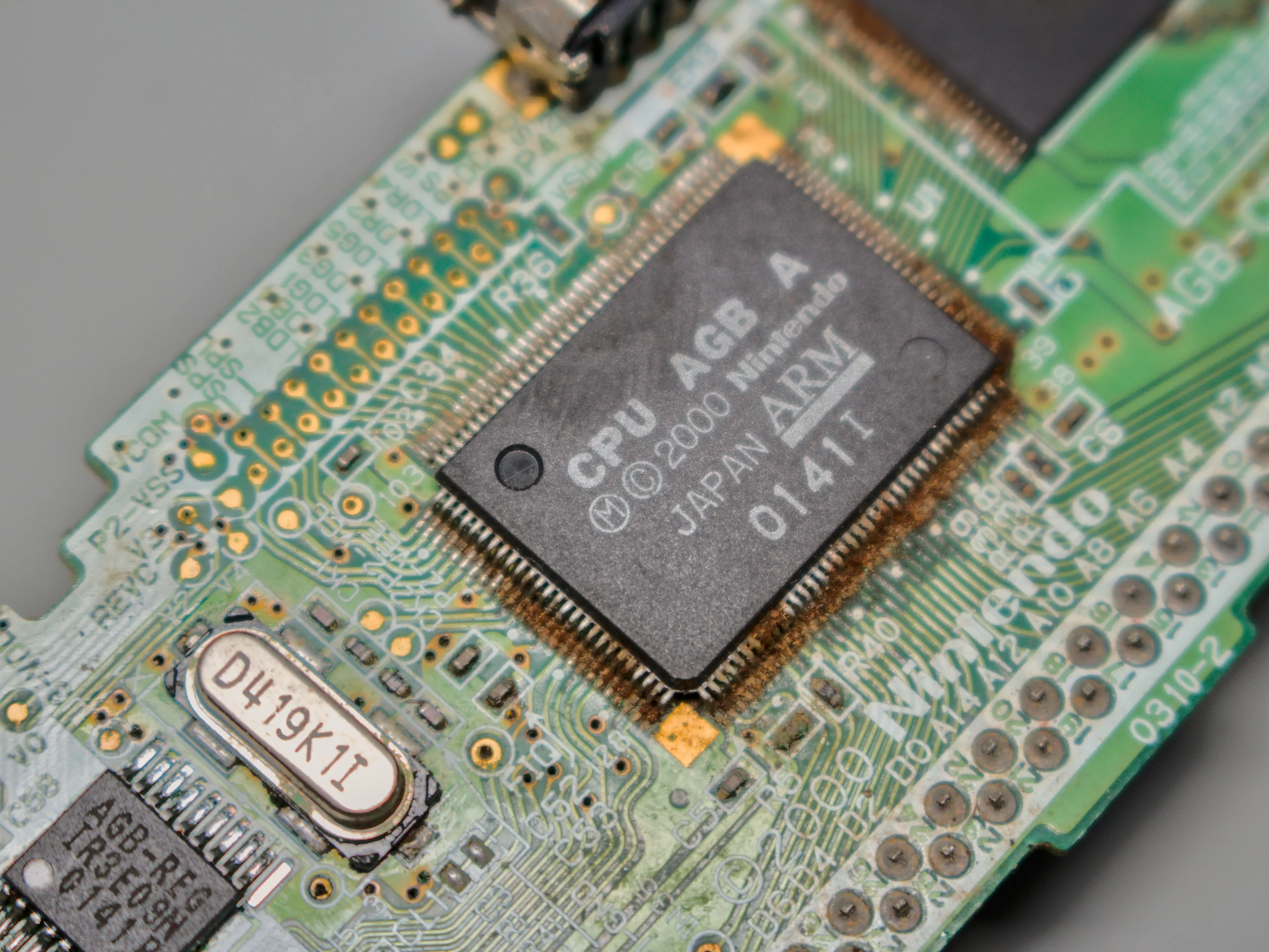 Close-up of the Game Boy Advance CPU with heavy corrosion around the chip pins and surrounding traces