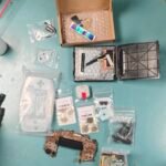 Parts gathered for a Game Boy Advance rebuild, including the motherboard, clear shell, replacement screen, buttons, batteries, and small components