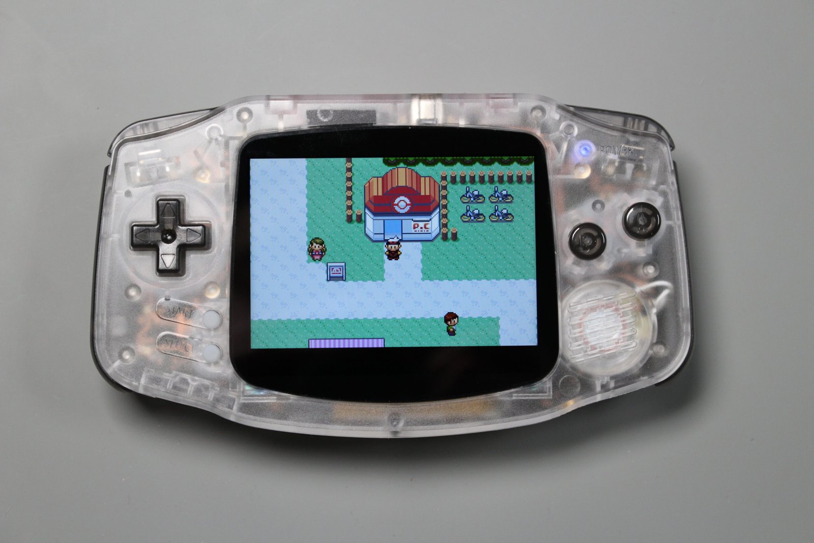Clear-shell Game Boy Advance powered on and displaying a Pokémon game